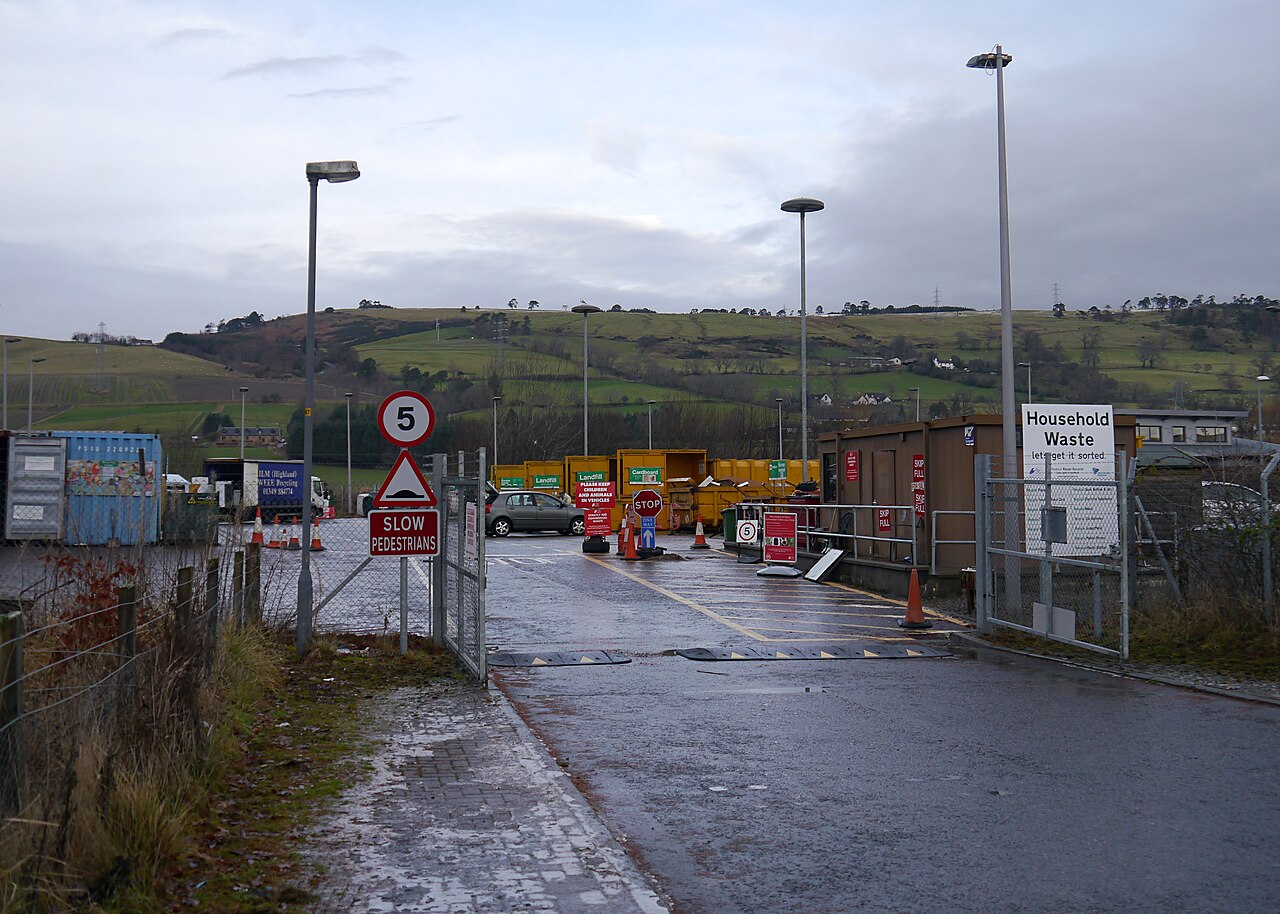 Entrance to Dingwall Recycling Centre in the Highlands, with a Household Waste sign, skips and green hills behind