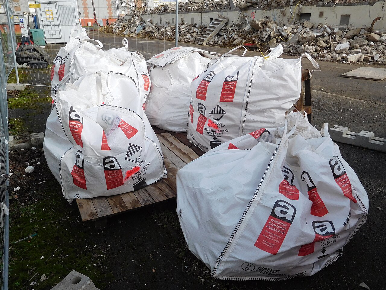 Asbestos waste packed in large white bags printed with the asbestos warning symbol, stacked on a pallet